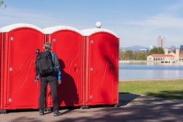 Red portable restrooms placed along a lakefront path with the skyline behind